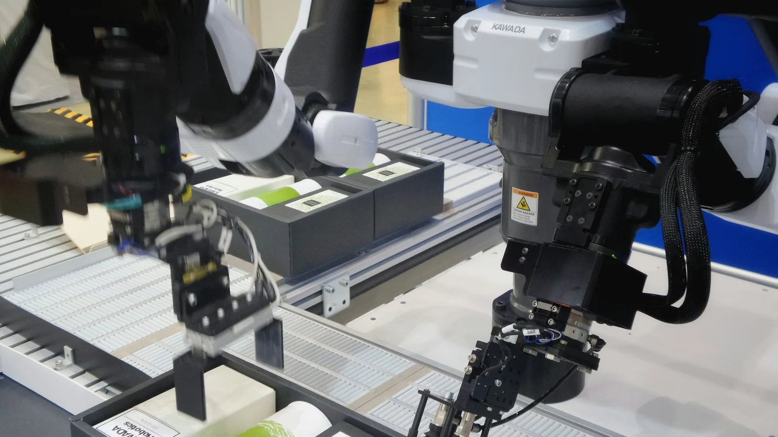 Two robot arms with grippers pick items out of boxes on a conveyor.